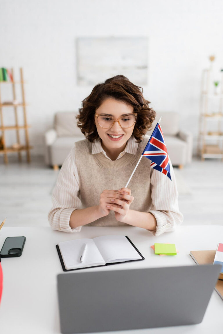 Uśmiechnięta nauczycielka z flagą UK podczas korepetycji z angielskiego online dla dorosłych